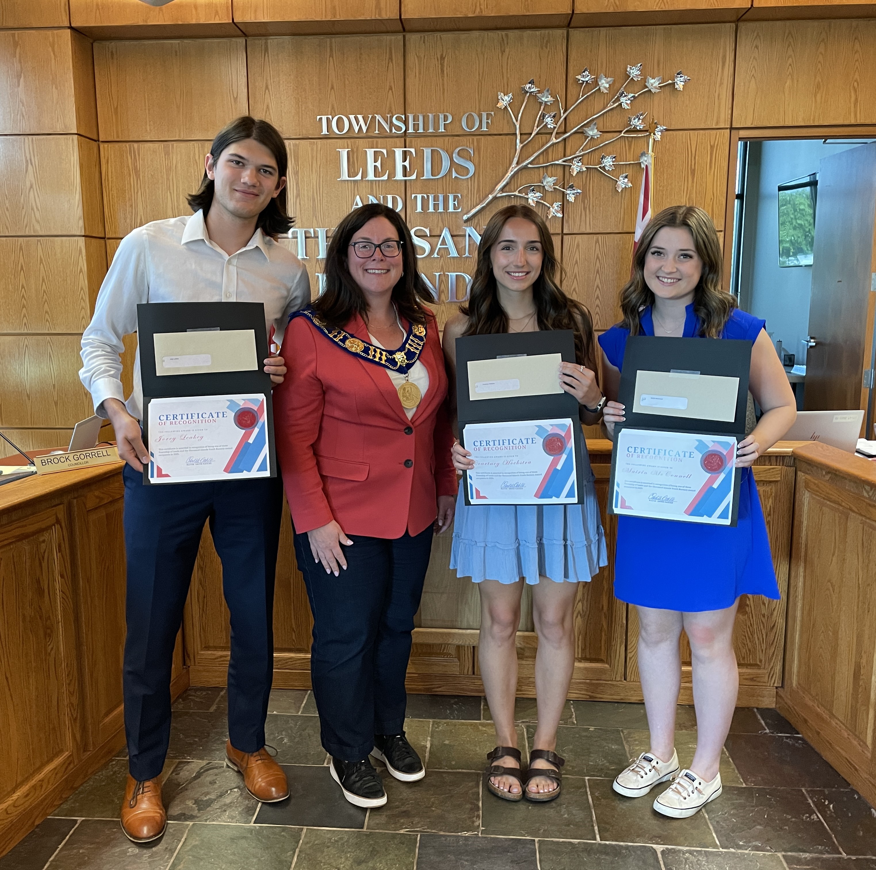 Four young adults holding certificates