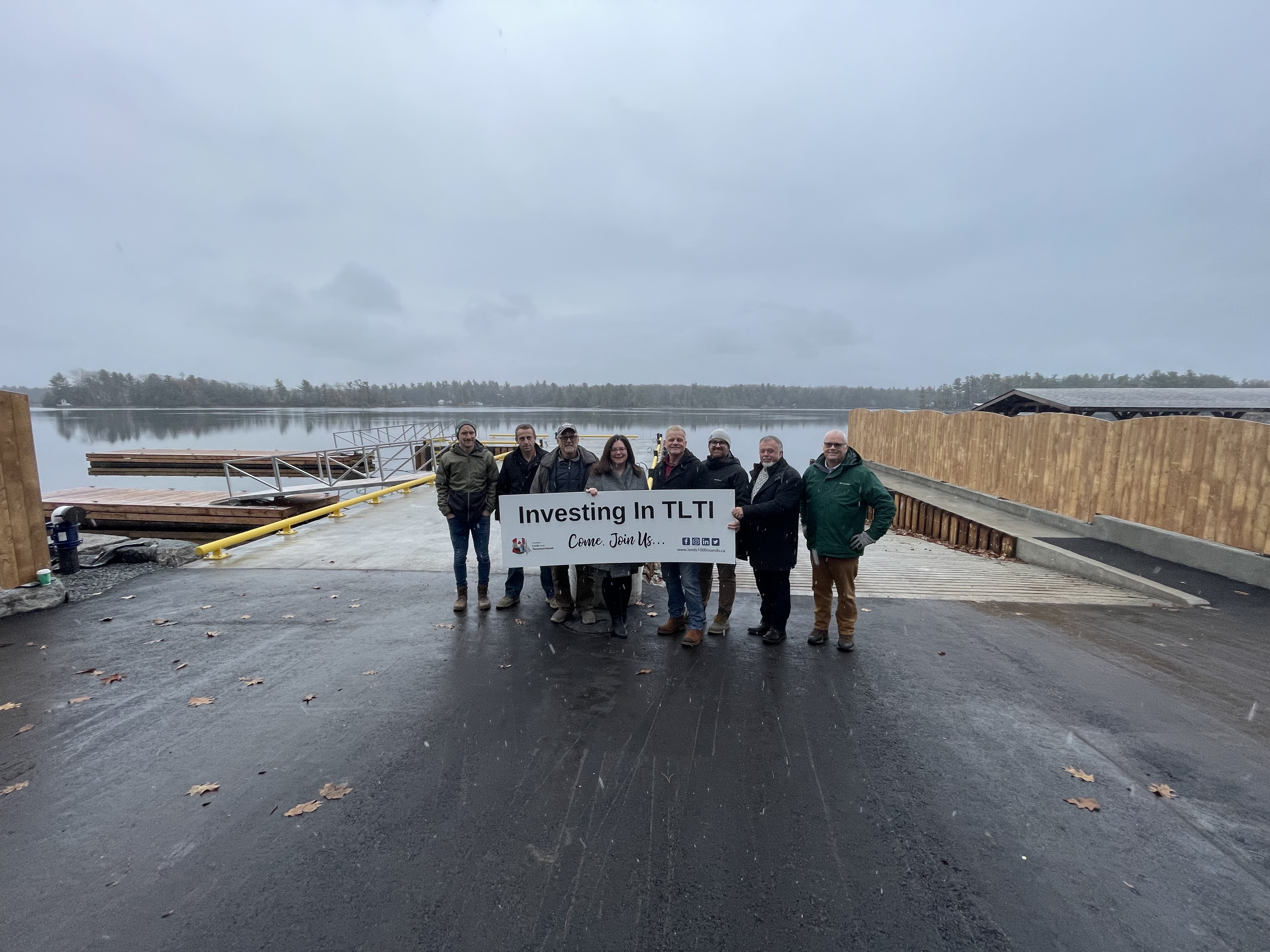 People standing on a wharf holding a sign that says TLTI investing in the future