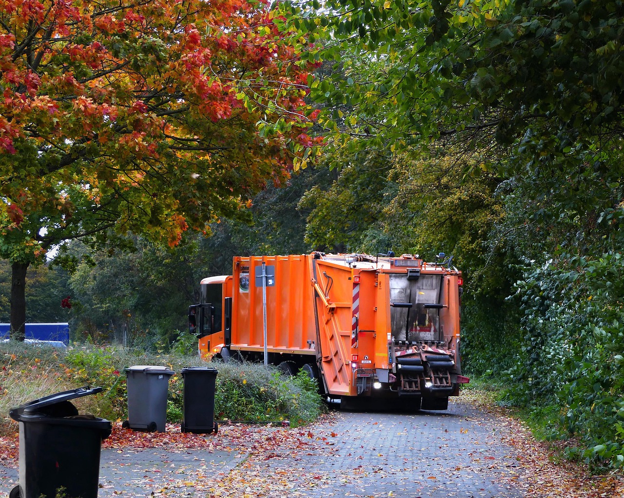 Orange garbage truck picking up garbage from a road in the fall