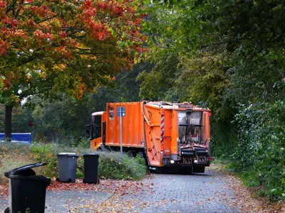 Orange garbage truck picking up garbage from a road in the fall