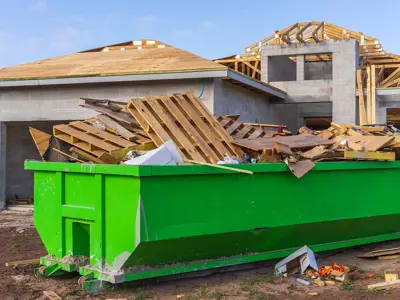 large construction waste bin with construction waste material, with a house being constructed in the background